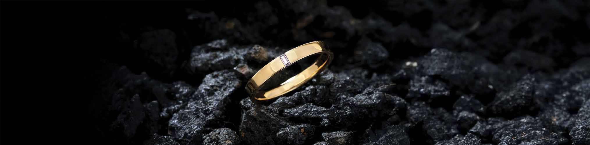 Polished yellow gold men's wedding ring on black volcanic stone, masculine modern jewellery ring