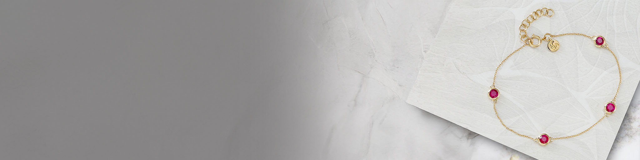 Fine yellow gold bracelet set with red rubies on white marble, delicate jewellery with coloured gemstones