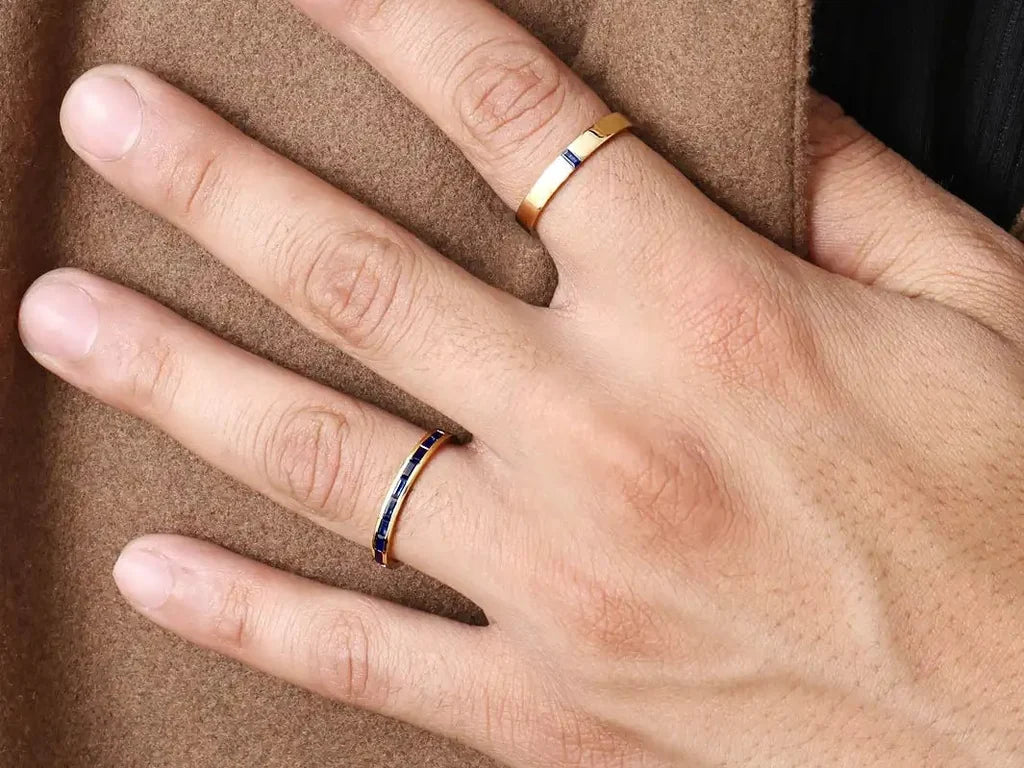 Two Mayuri men's engagement rings in 18ct yellow gold set with sapphires, worn on the hand