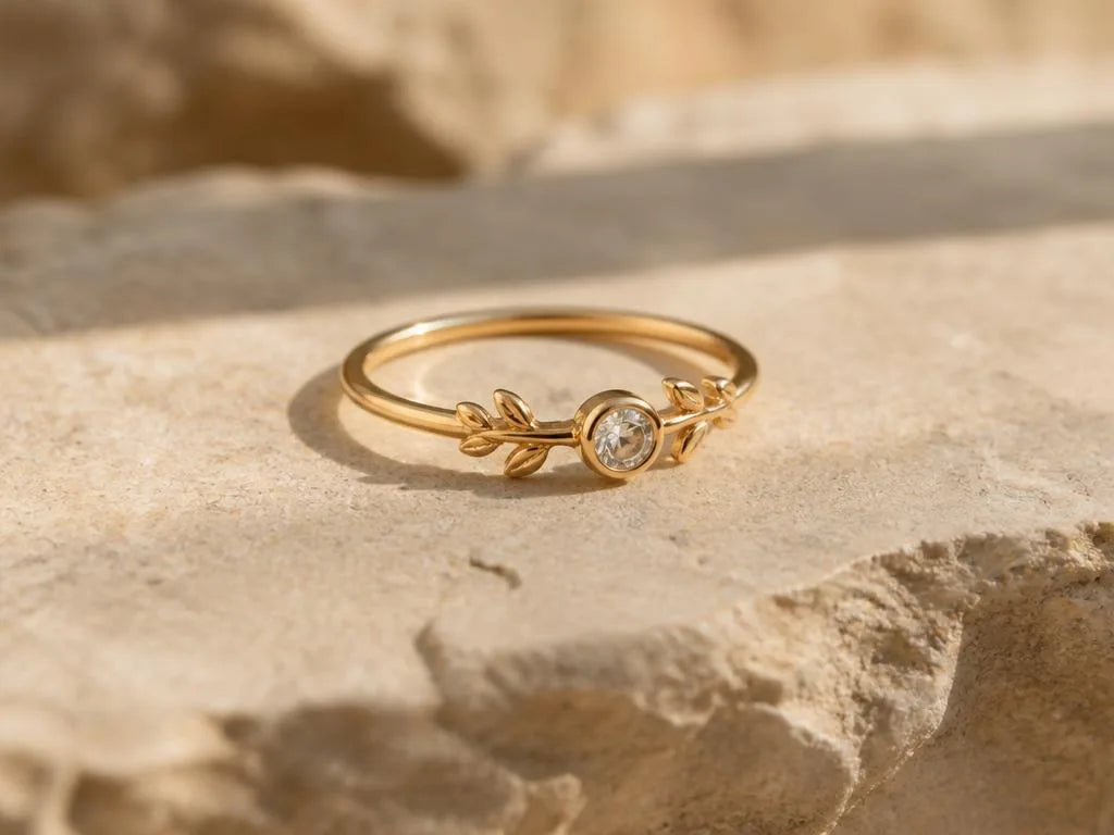 A delicate 18ct yellow gold ring featuring a diamond and leaf motif, resting on a natural stone surface, a romantic design by Mayuri