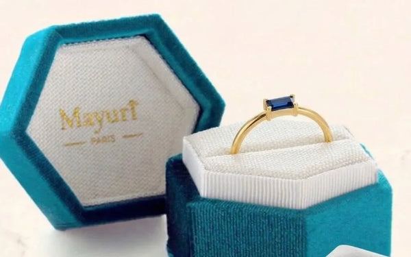 Bague saphir en or jaune dans son écrin Mayuri en velours, à côté du chiffon de polissage