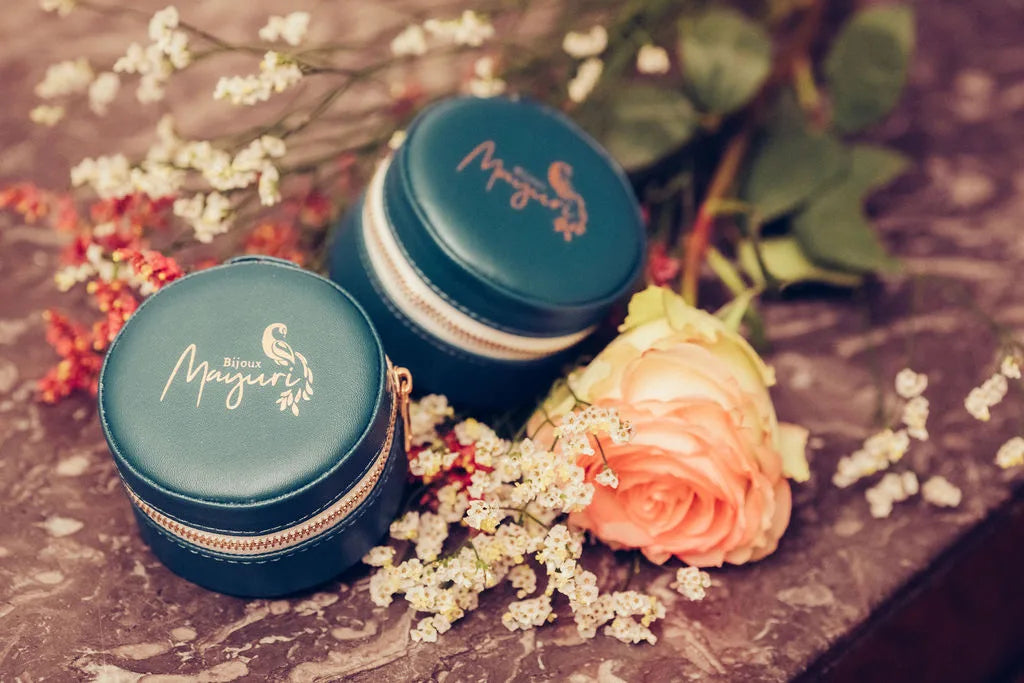 Two round Mayuri turquoise velvet jewellery cases placed on a lifestyle background with dried flowers and roses