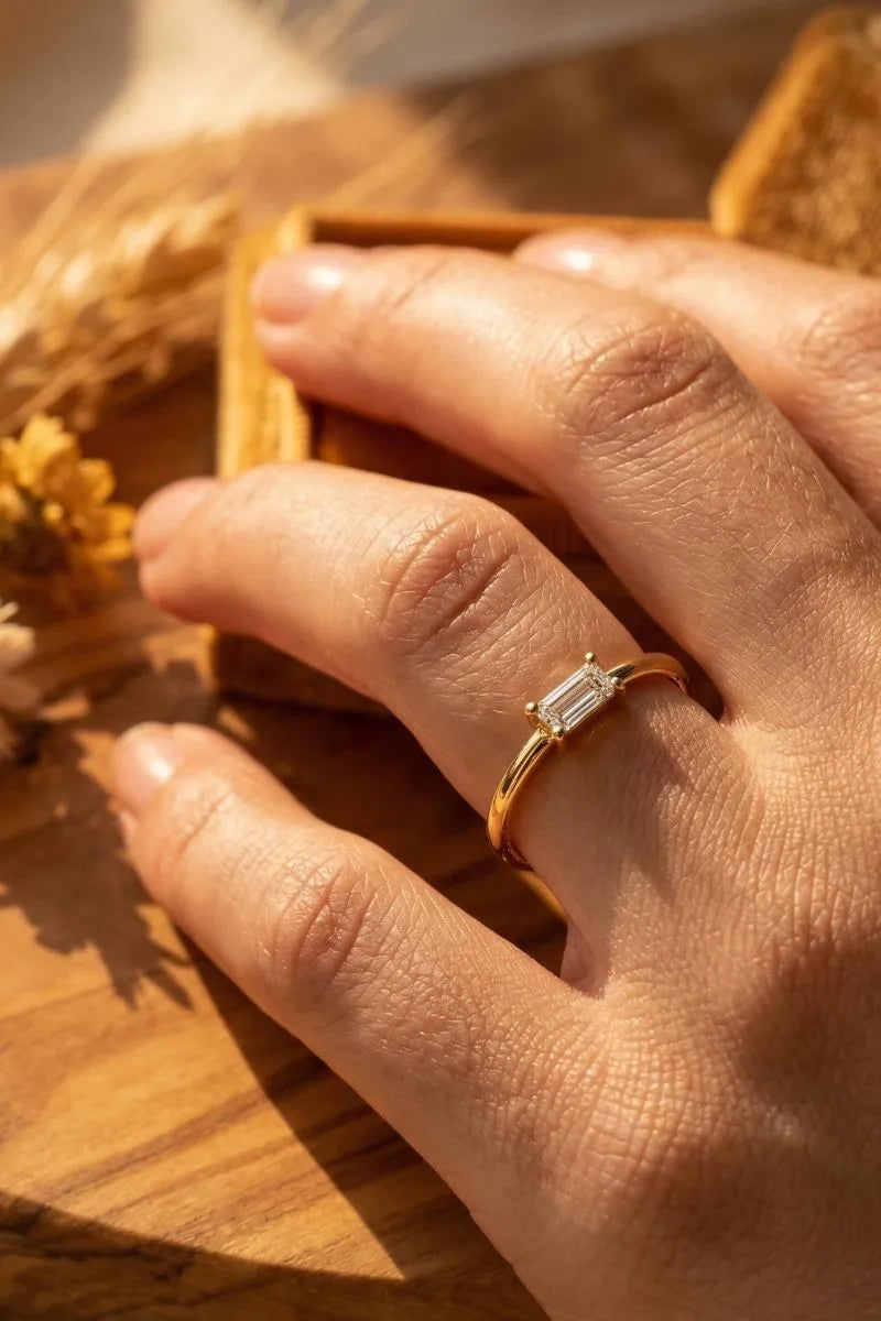 18ct yellow gold baguette cut diamond solitaire ring worn on the finger against a natural background, by Mayuri