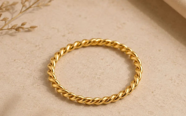 Twisted Musubi wedding ring in 18K yellow gold placed on natural beige background by Mayuri