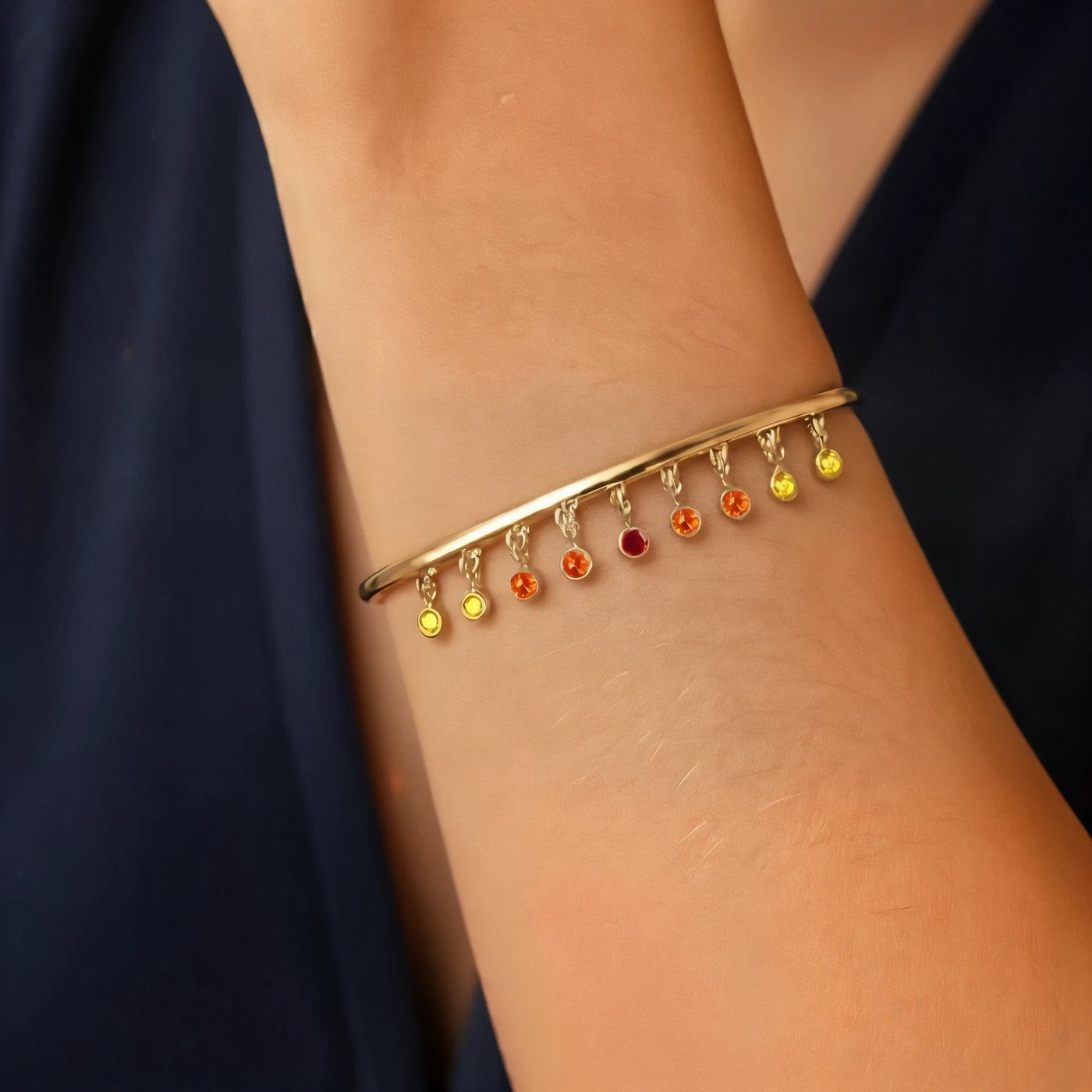Jonc Megha saphir sunset en or jaune 18 carats porté au poignet, dégradé de saphirs orange et jaunes