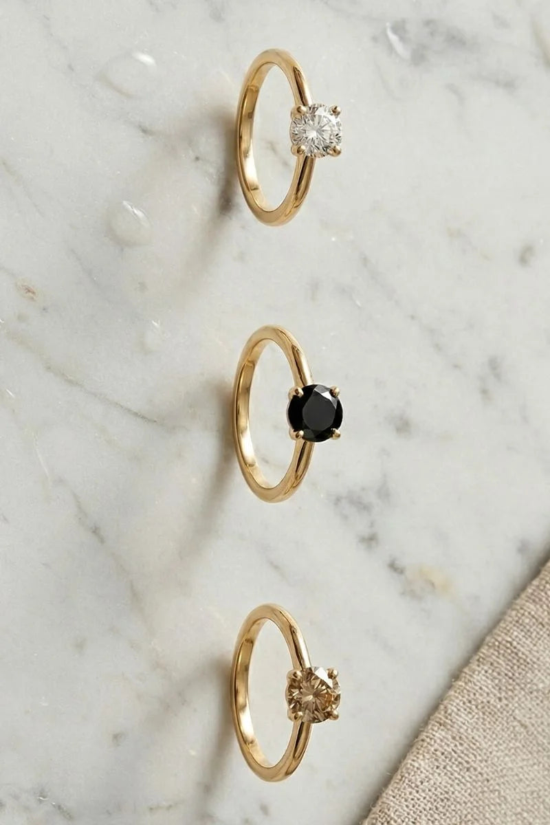 Three solitaire rings in yellow gold: white diamond, black diamond and champagne diamond
